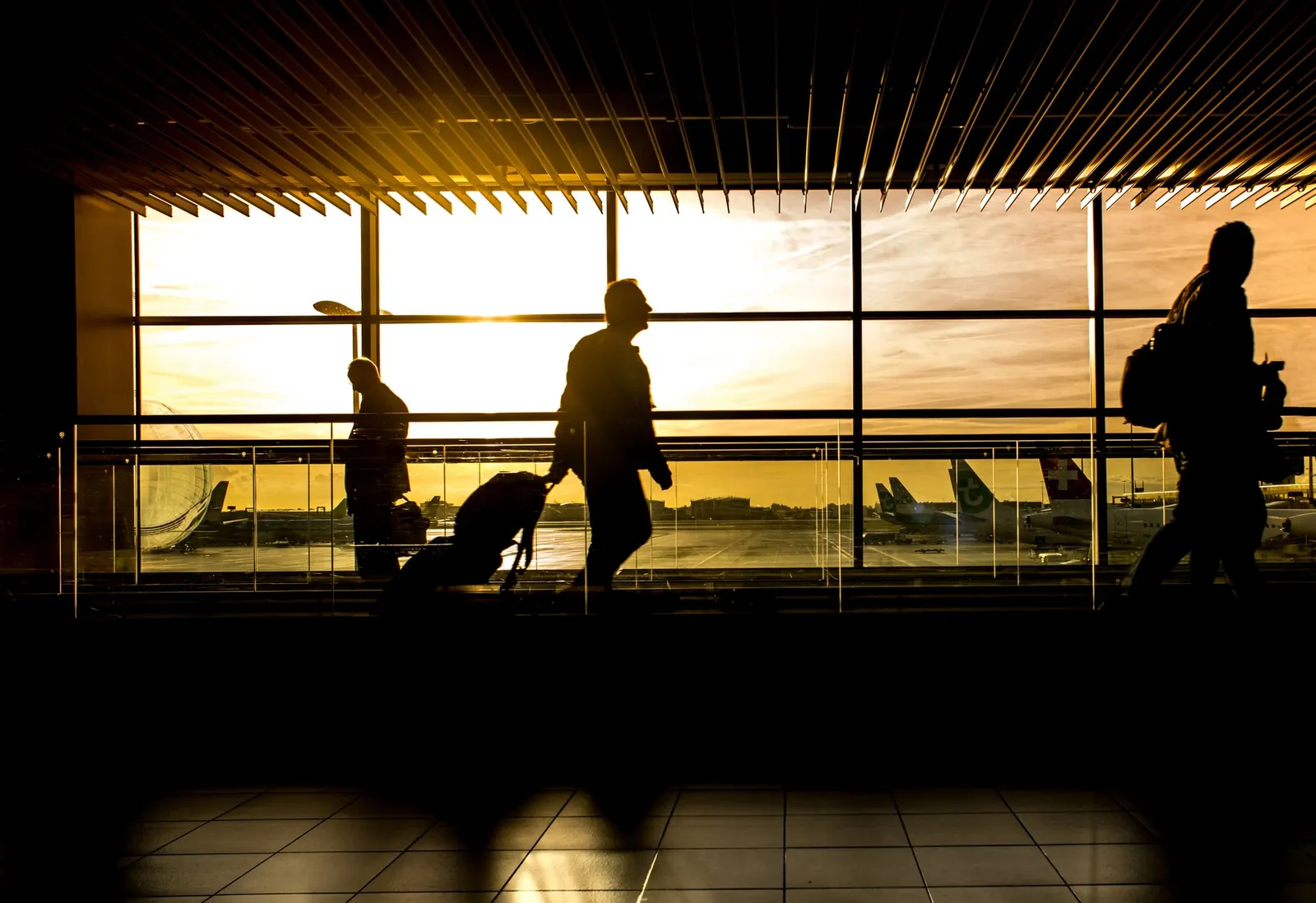 Travellers with luggage silhouetted in an airport at sunset